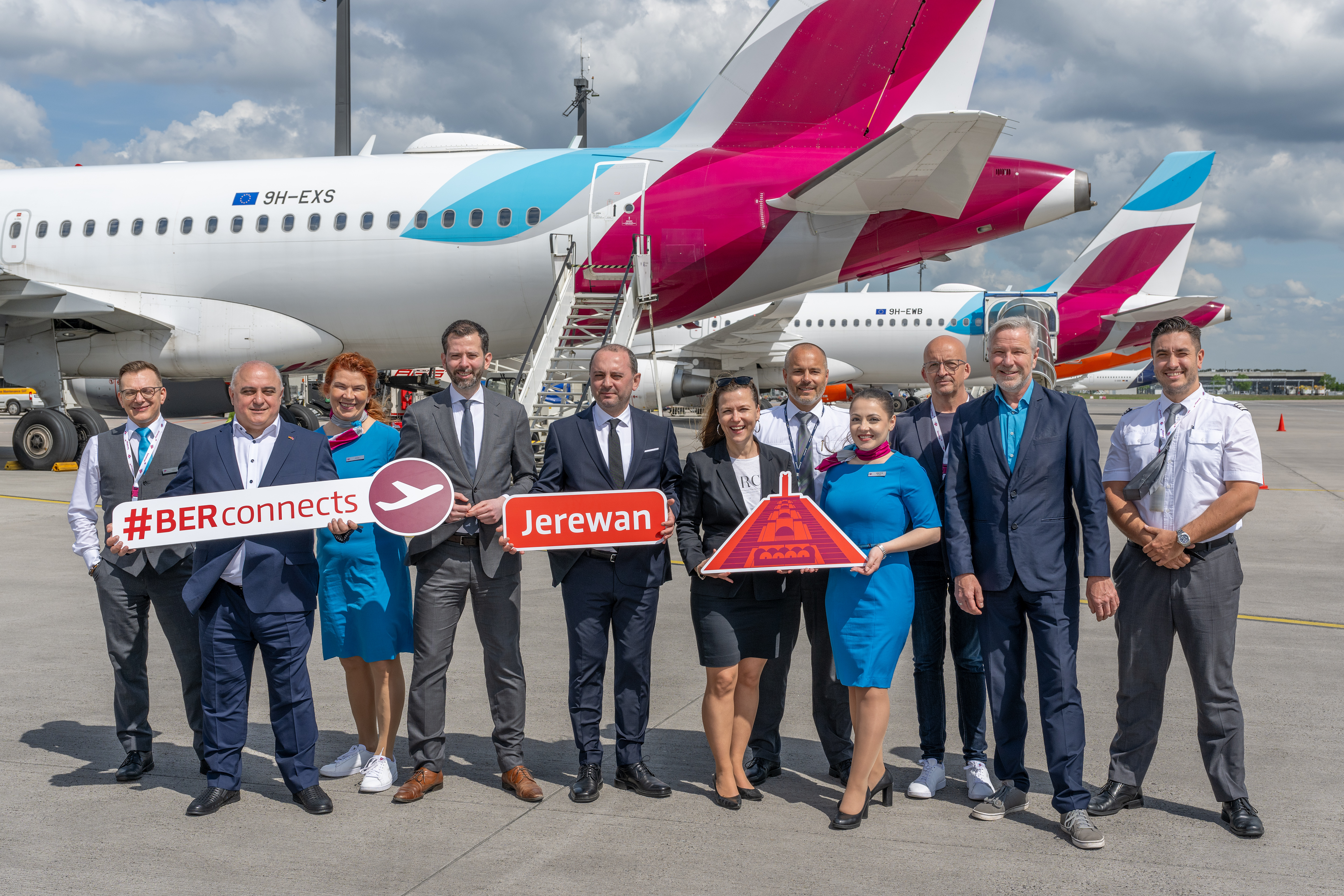 Eine Eurowings-Crew und weitere Personen vor einem Flugzeug, alle lächeln in die Kamera und halten Schilder in den Händen. Darauf steht "#BER connects", "Jerewan" © Günter Wicker / FBB
