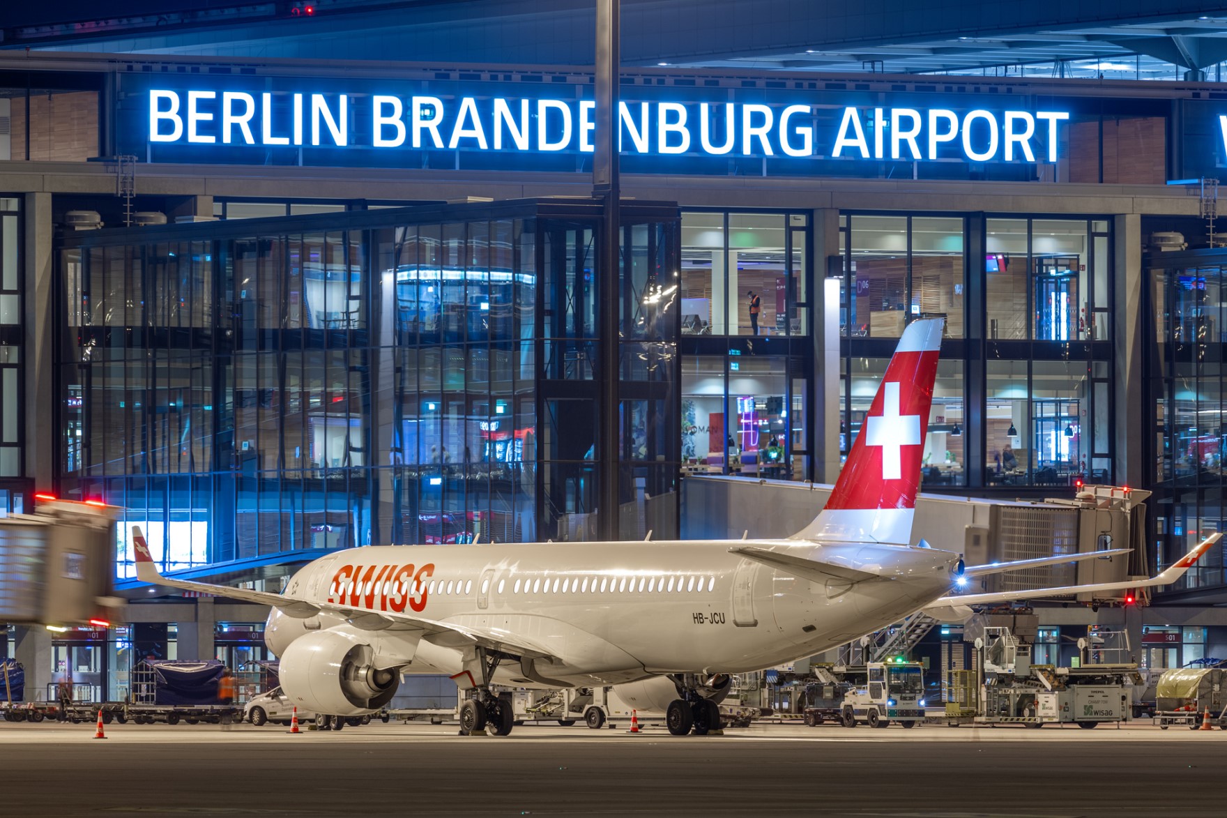 Ein Flugzeug von Swiss International Air Lines steht nachts auf dem Vorfeld vor dem beleuchteten BER-Terminal.