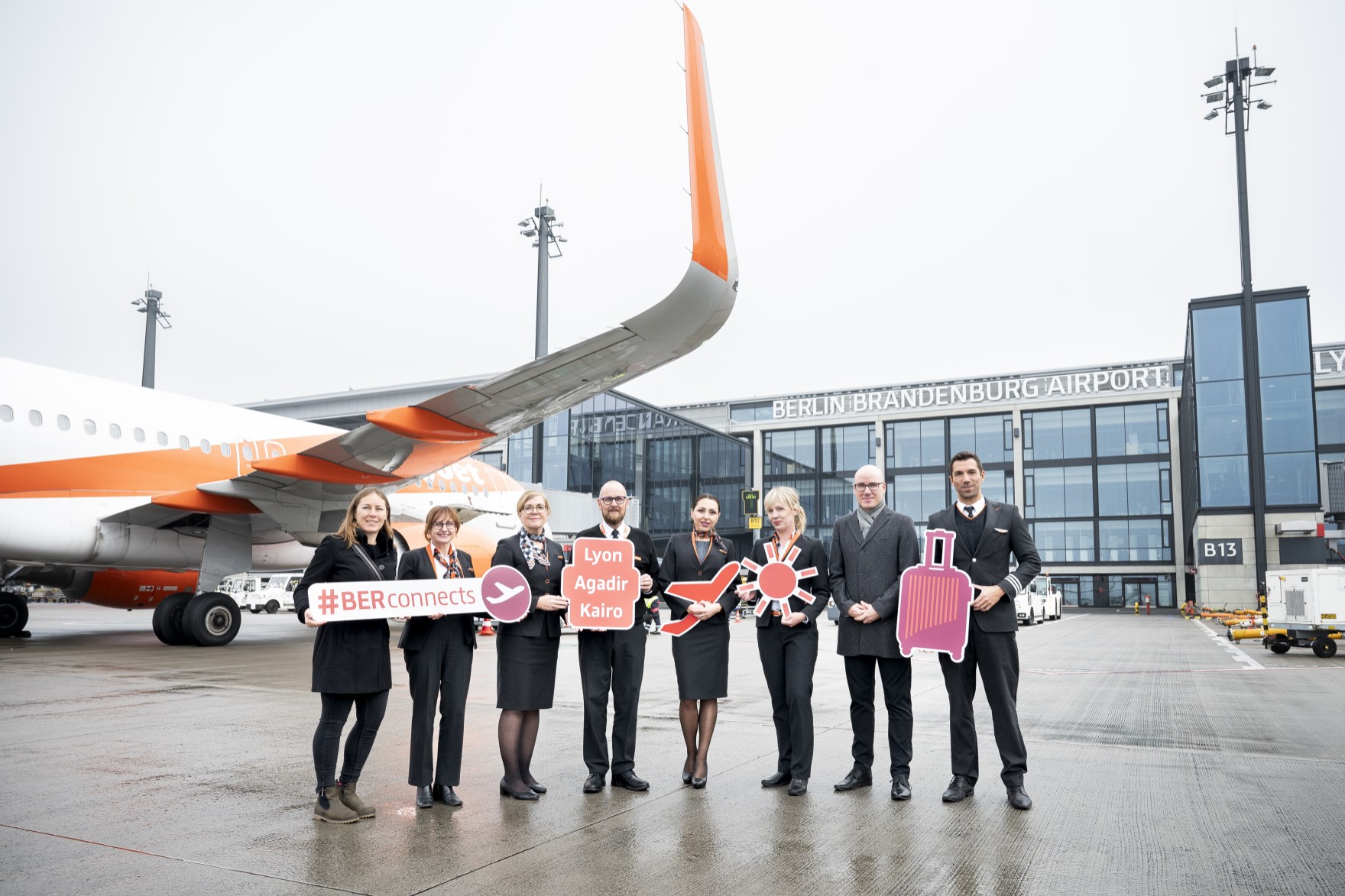 Eine Gruppe von Personen posiert mit Schildern auf dem Vorfeld vor einem Flugzeug. 