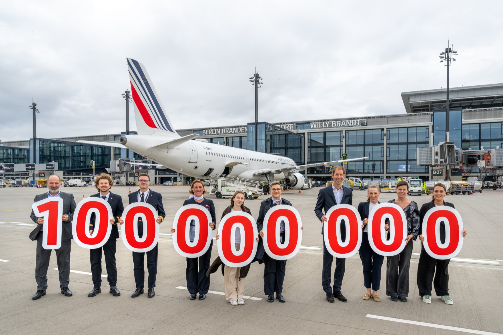Eine Gruppe von Personen posiert mit Schildern auf dem Vorfeld vor einem Flugzeug. In English: A group of people pose with signs on the apron in front of an aircraft.