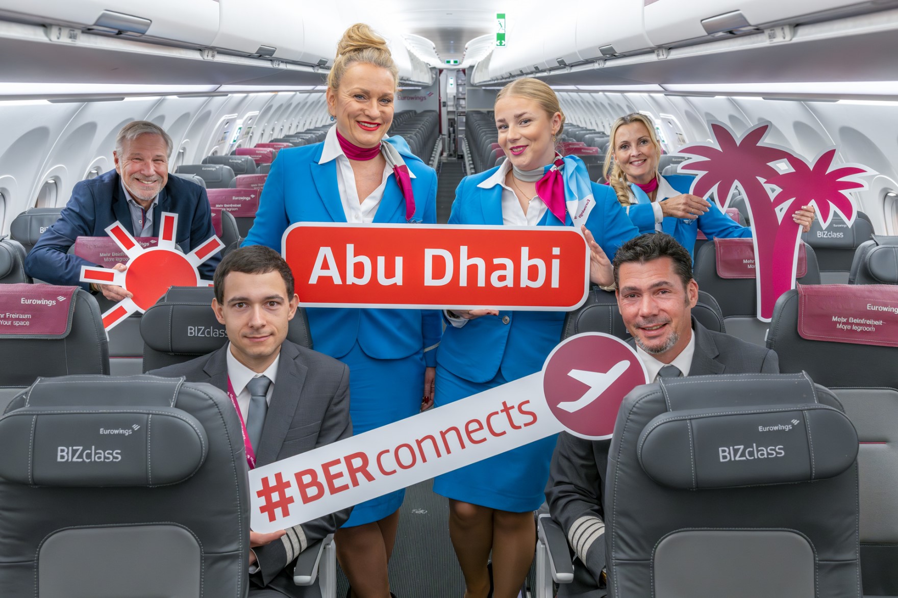 Eine Flugzeug-Crew posiert im Flugzeug mit Schildern, auf denen Abu Dhabi und #BERconnects steht.