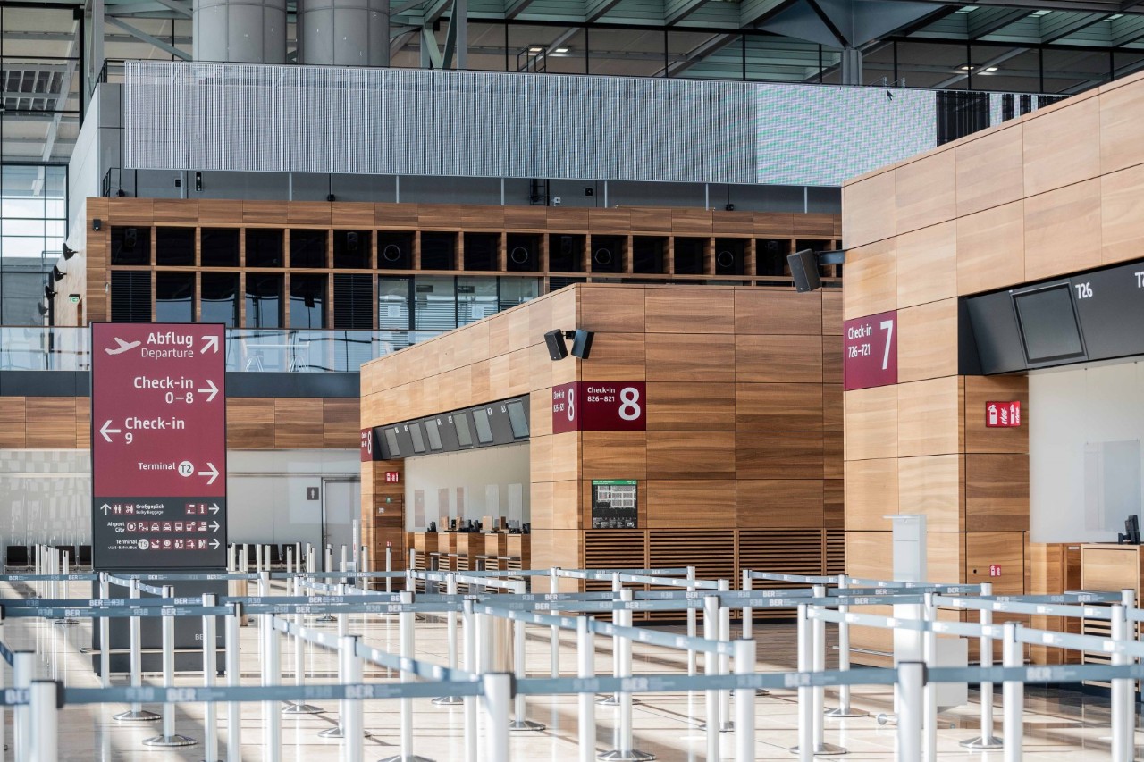 Check-in-Counter holzfarben. Daneben Tensatoren und ein Wegweiser.