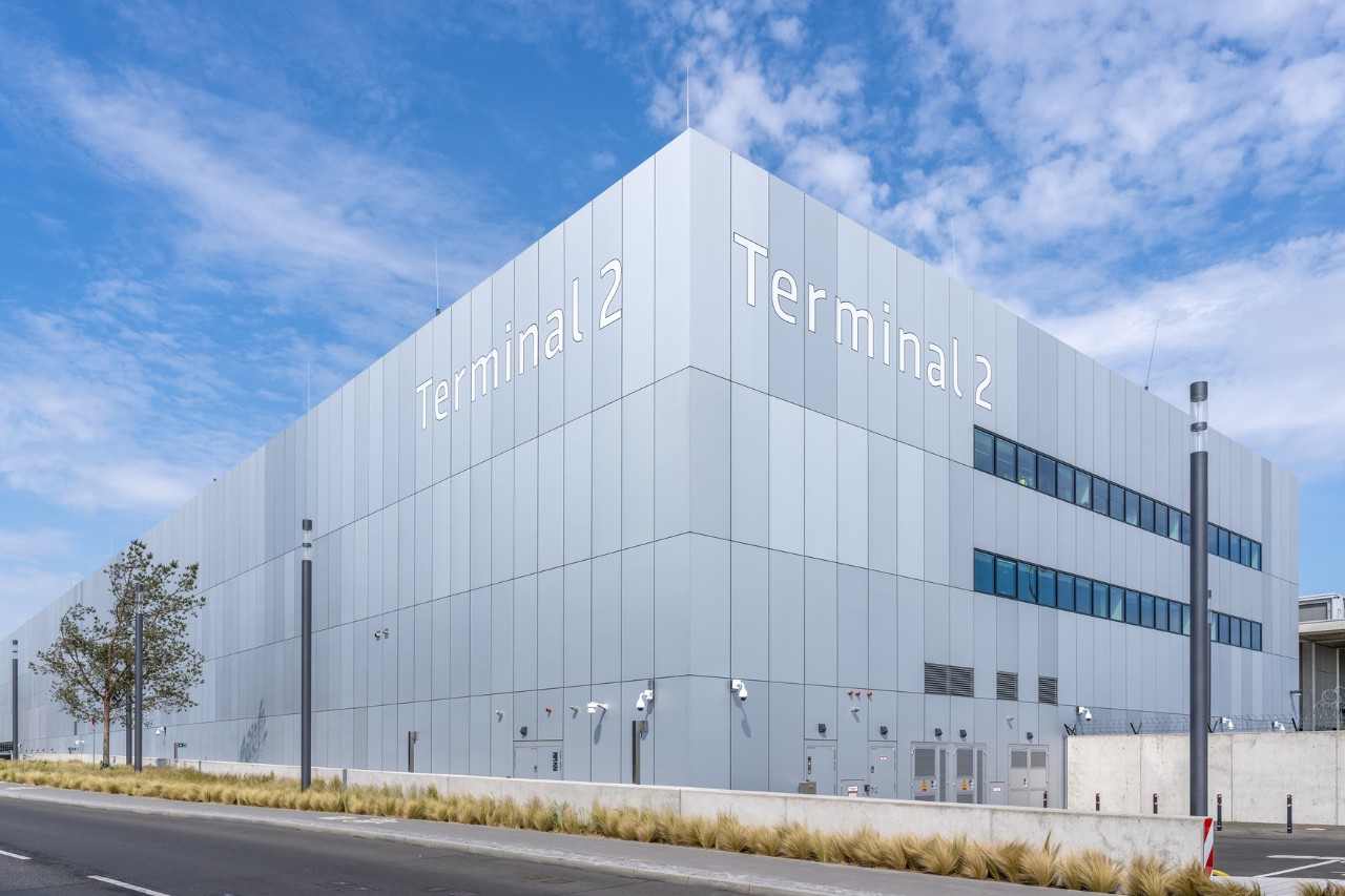 Das Terminal 2 von außen. Davor eine Straße und Bäume.