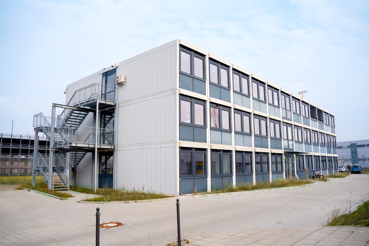 Ein Gebäude. 3 Stockwerke. Davor ein Gehweg.