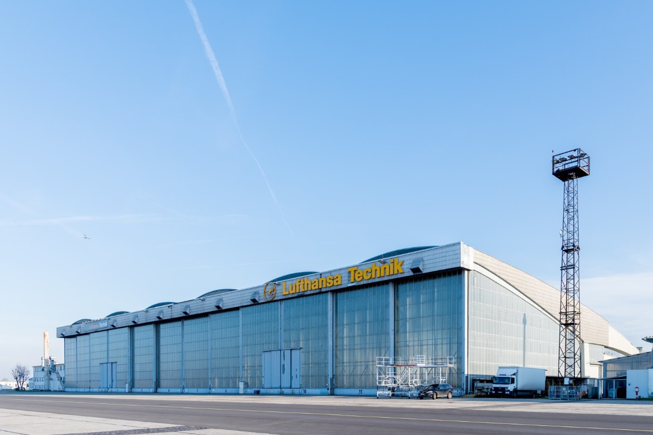Ein Hangar mit dem Schriftzug Lufthansa Technik. Daneben ein Lichtmast. Davor Vorfeld.