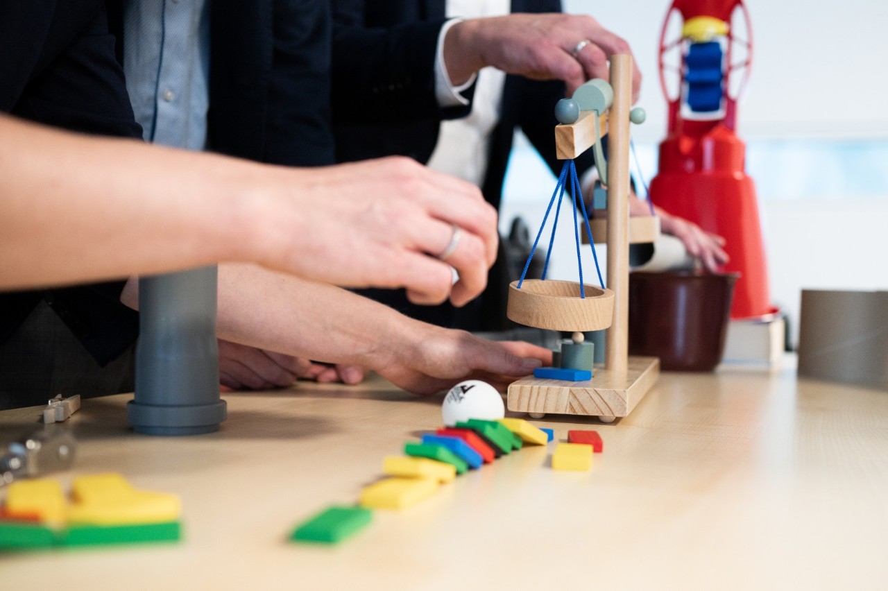 Mehrere Menschen stehen um einen Tisch herum. Auf diesem befinden sich Geräte für Teamwettbewerbe