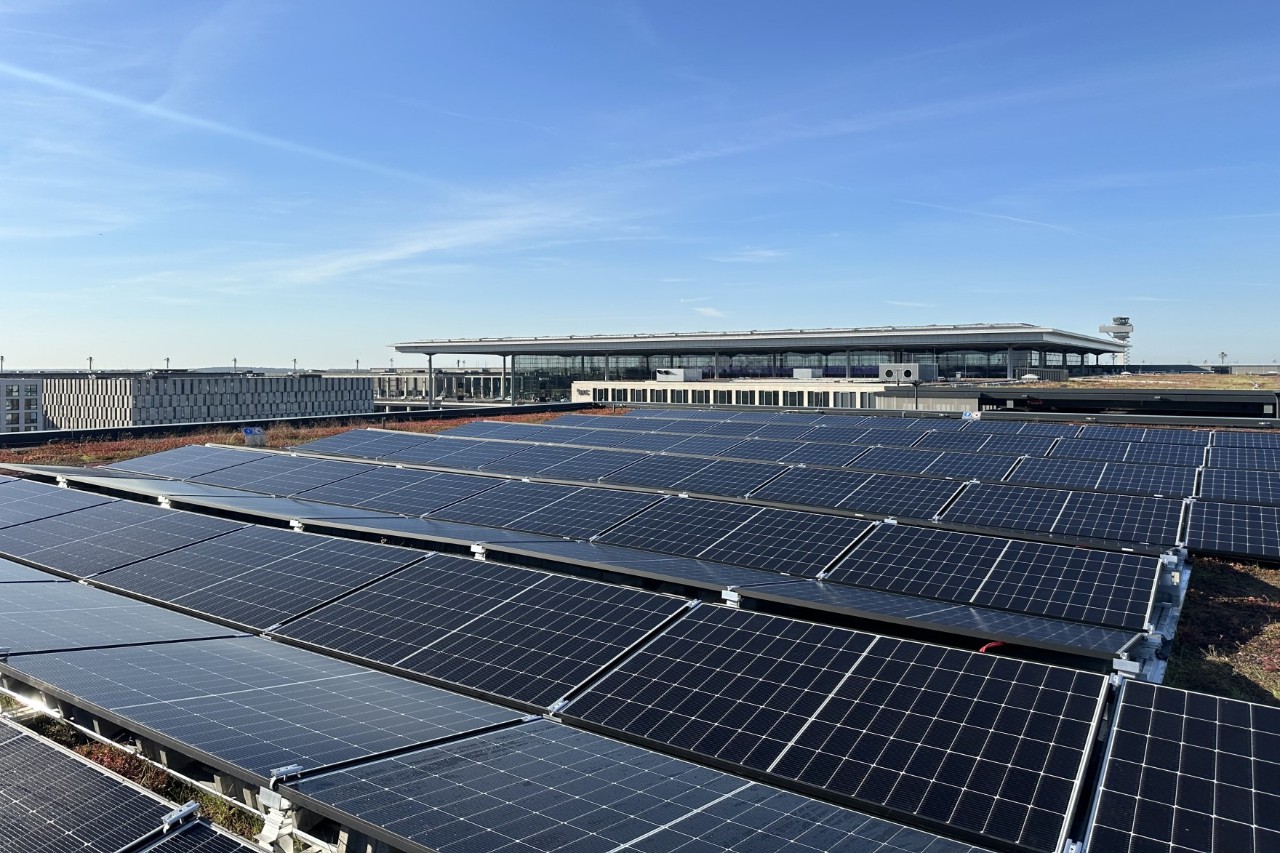 Photovoltaik-Paneele auf einem Dach. Im Hintergrund ist das Terminal 1 des BER zu sehen.