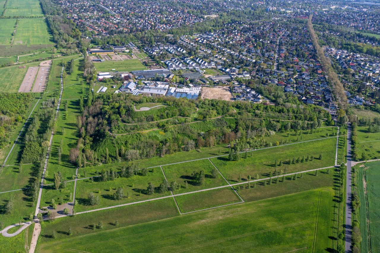 Luftbild, das eine große Siedlung und daran angrenzende Wiesen mit Bäumen zeigt