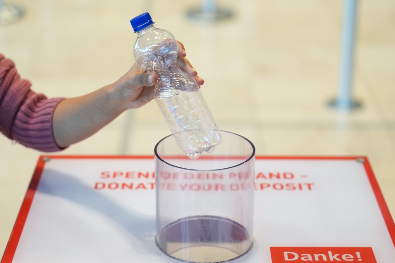 Eine leere Plastikflasche wird in einen Pfandsammelbehälter geworfen.