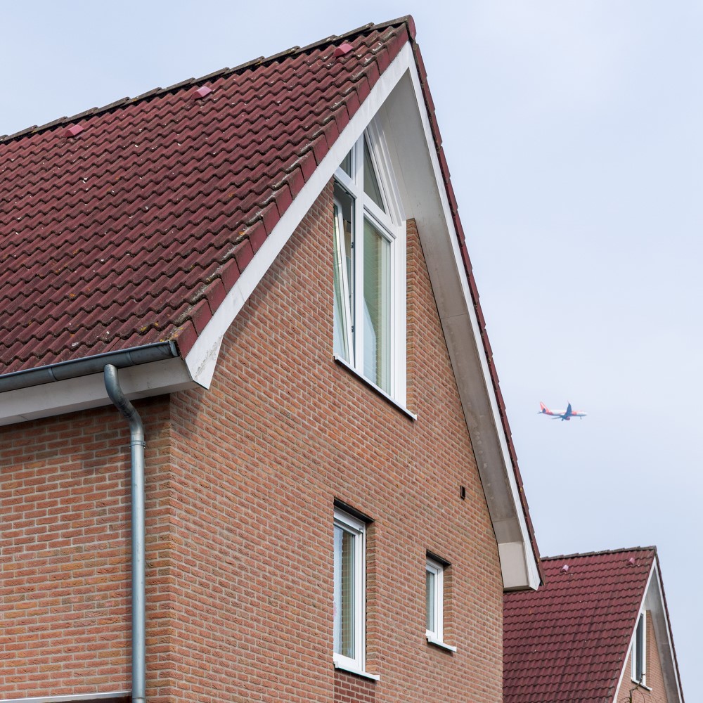 Zwei Einfamilienhäuser. Am Himmel über ihnen fliegt ein Flugzeug.