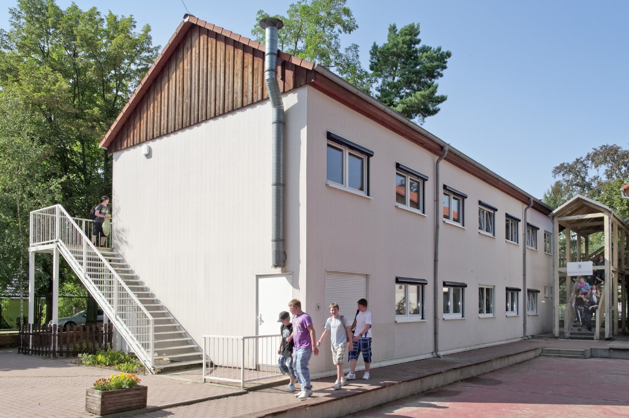 Mehrere Schulkinder mit Rucksäcken vor einem zweistöckigen Gebäude