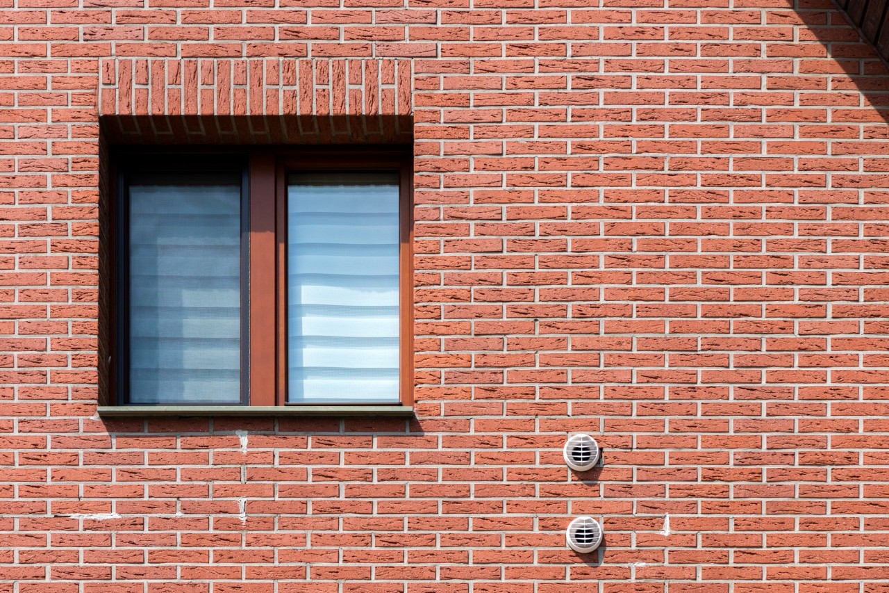Hausfassade aus Backstein mit einem Fenster und in der Wand angebrachten Belüftungsvorrichtungen