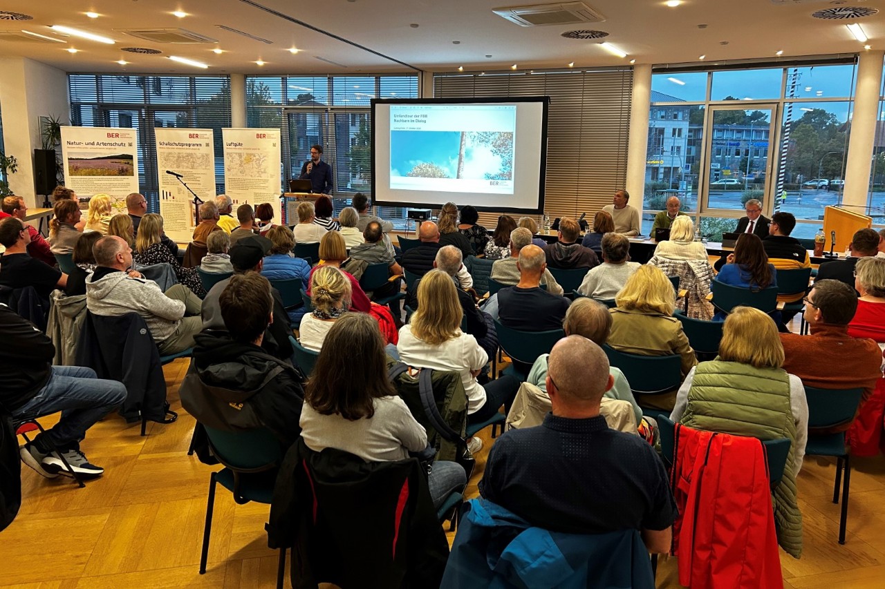 Ein großer Raum voller Menschen, die auf Stühlen sitzend einer Präsentation folgen.