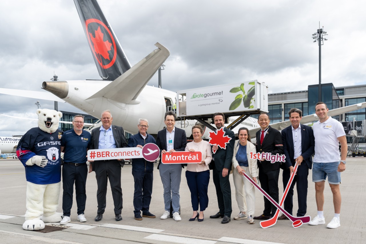 Eine Gruppe Menschen hält vor einem Flugzeug der Fluggesellschaft Air Canada Schilder in den Händen und posieren für ein Foto.