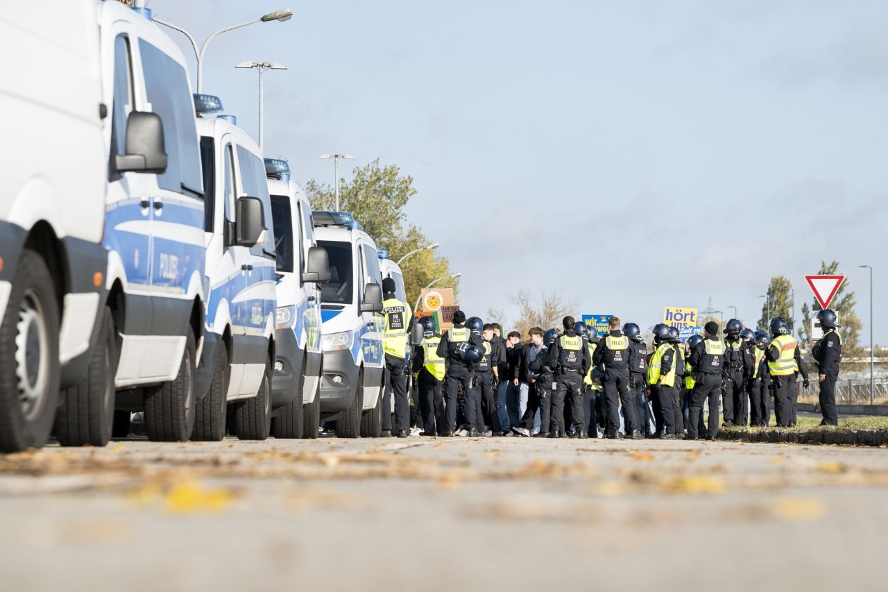 Mehrere Polizeiautos und eine Gruppe in schwarz gekleideter Personen mit gelben Warnwesten