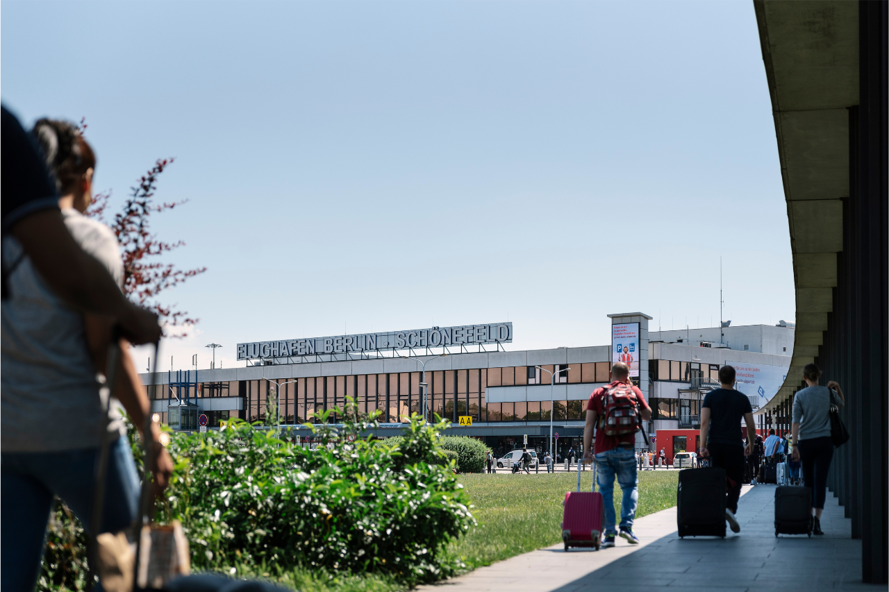 Personen laufen unter einem Wandelgang zum Gebäude des ehemaligen Schönefelder Flughafens