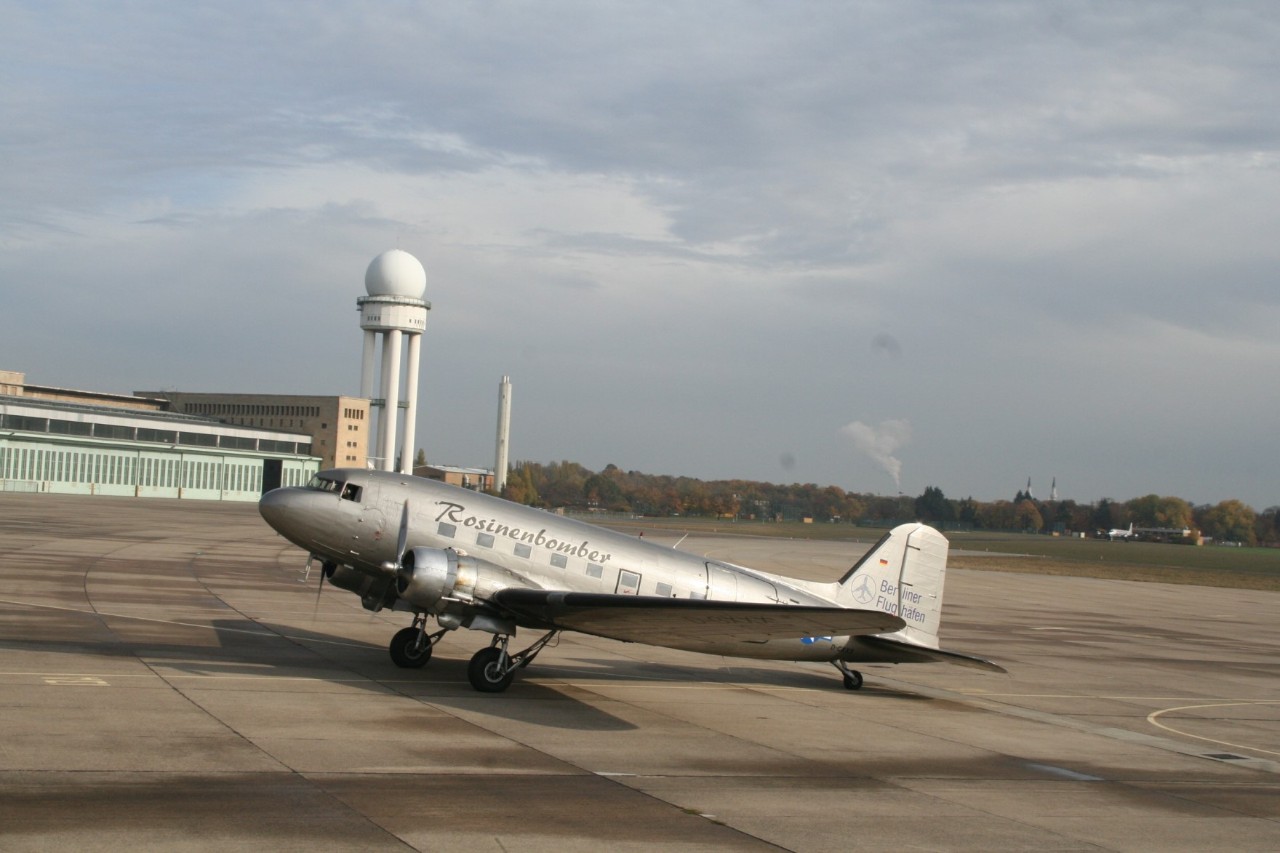 Ein Rosinenbomber steht auf dem Vorfeld des Flughafens Tempelhof. Dahinter der Wasserturm und die Hangar.