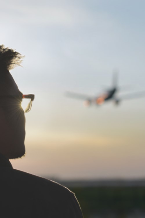 Mann schaut im Sonnenuntergang einem Flugzeug hinterher