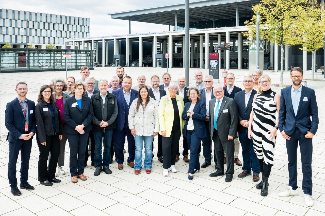 Eine große Gruppe Menschen posiert vor einem Flughafengebäude
