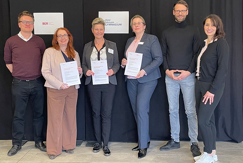 Sechs Personen auf einer Bühne, drei halten einen Vertrag in der Hand.