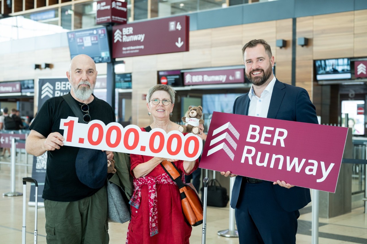 Drei Personen mit Schildern in der Hand vor dem BER Runway 