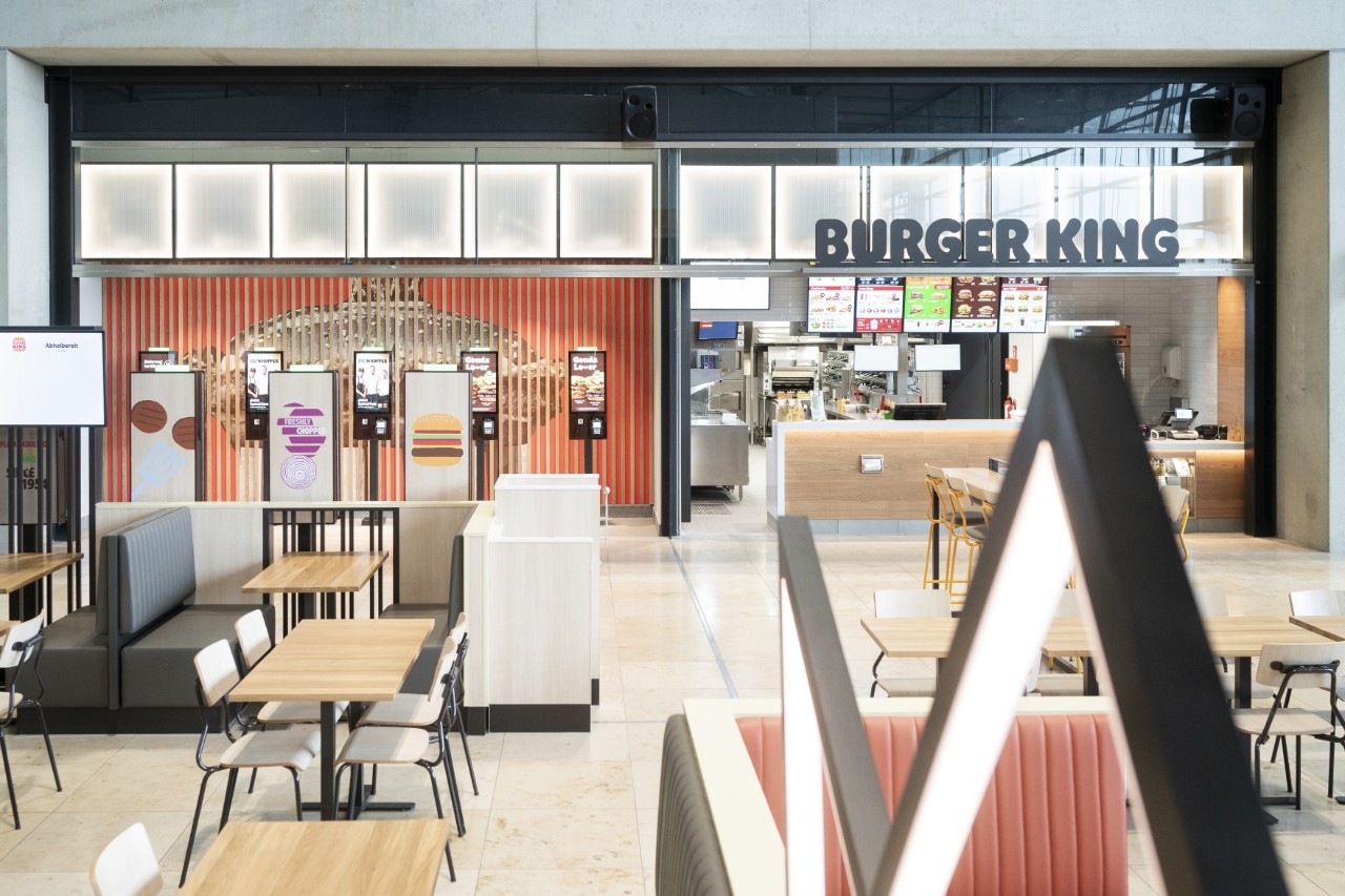 Burger King Filiale mit Theke und Bestellterminal; im Vordergrund Tische und Stühle