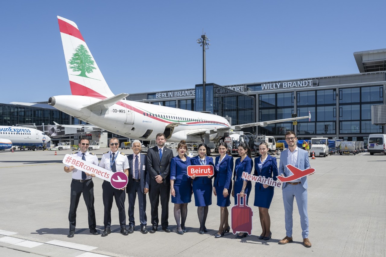 Eine Gruppe Menschen hält vor einem Flugzeug der Fluggesellschaft Middle East Airlines Schilder in den Händen und posieren für ein Foto.