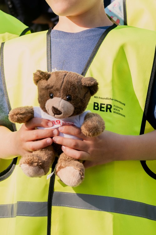 Detailaufnahme eines Kindes, das eine gelbe Warnweste trägt und einen Teddybären in den Händen hält