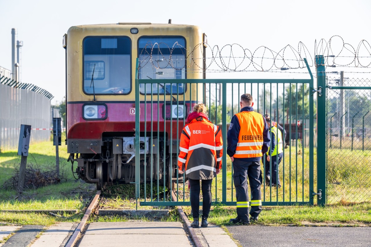 Two people in front of an old suburban railway behind a fence.