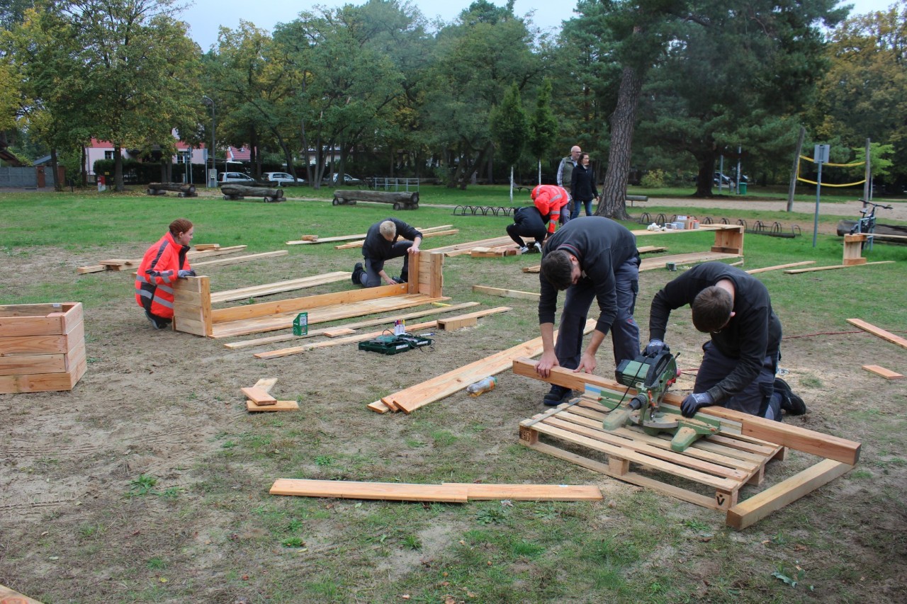 A small group is building something out of several boards in a meadow.