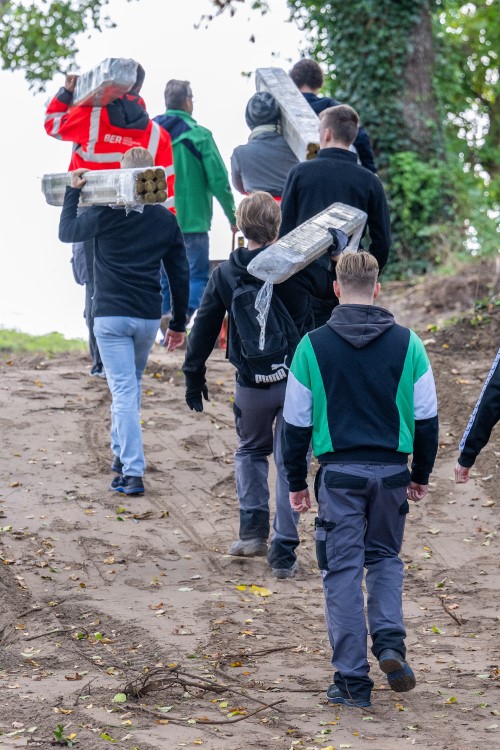 A small group is walking up a hill. Some of them have building materials on their shoulders.