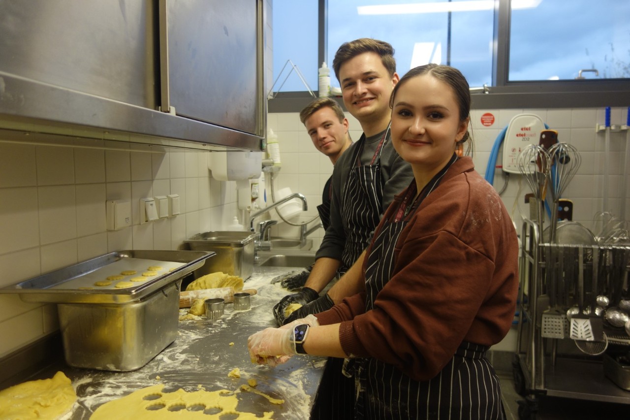 Three smiling young people cut out cookies.