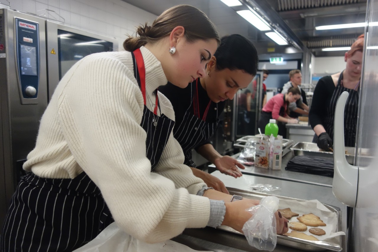 Several people are decorating cookies in a large kitchen.