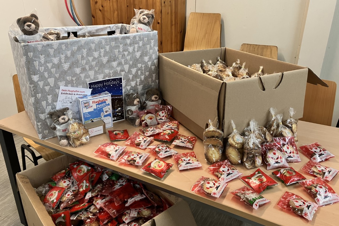 On a table and in several boxes are Christmas donations, including teddy bears, cookies and books.