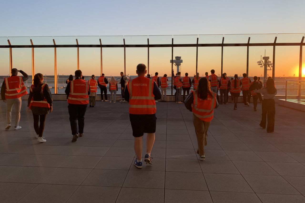Young people in orange vests on a large terrace at sunset.