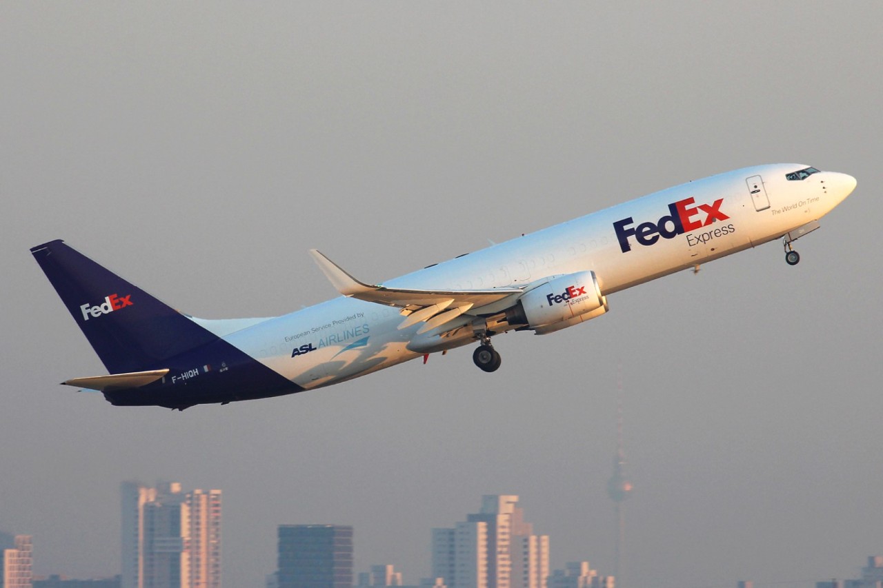 Ein FedEx Flugzeug beim Starten, im Hintergrund die Skyline von Berlin
