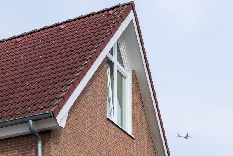 Facade of a detached house. An aeroplane is flying in the sky above.