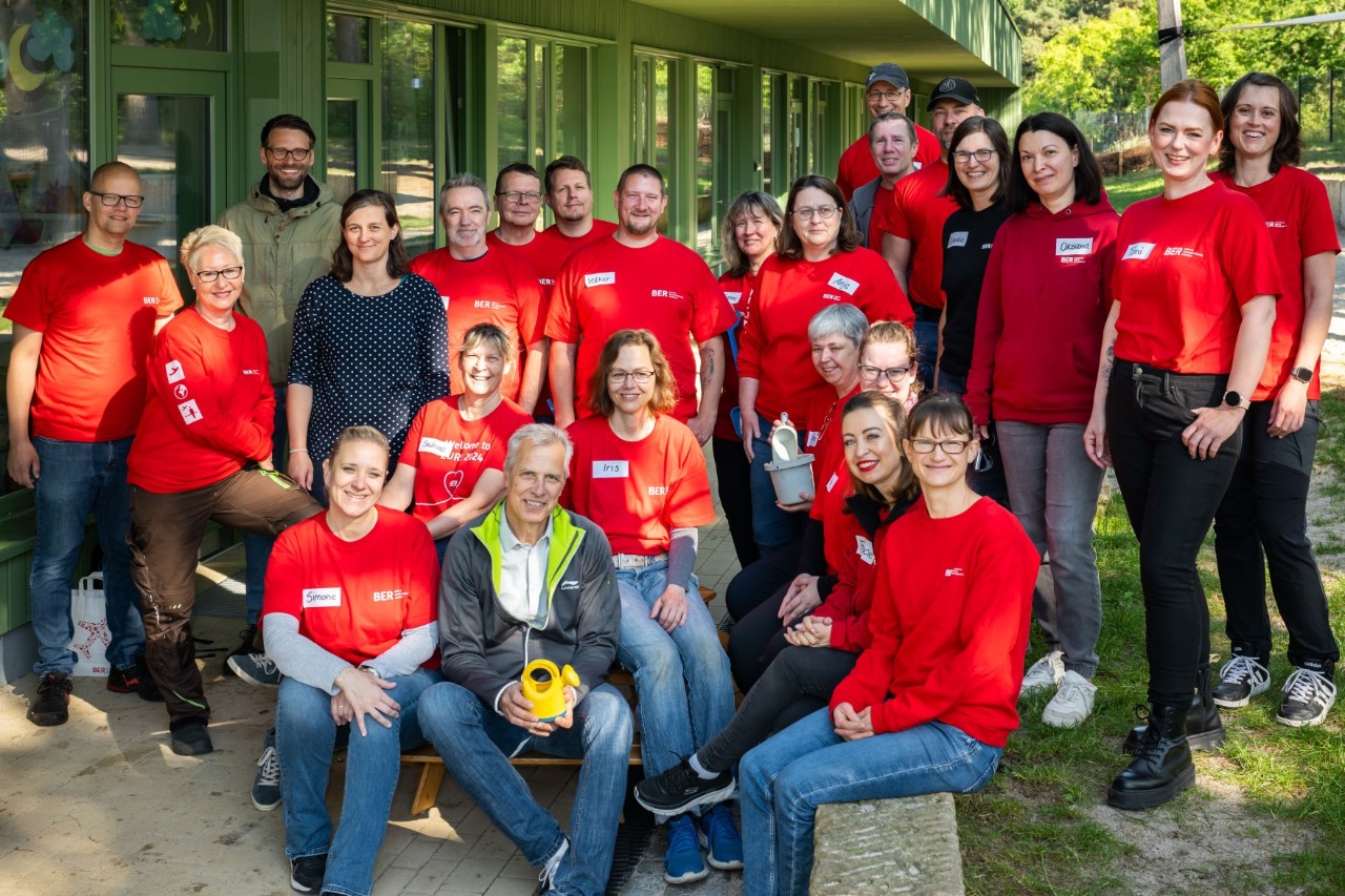 A group of people wearing red T-shirts and jumpers pose in front of a camera.