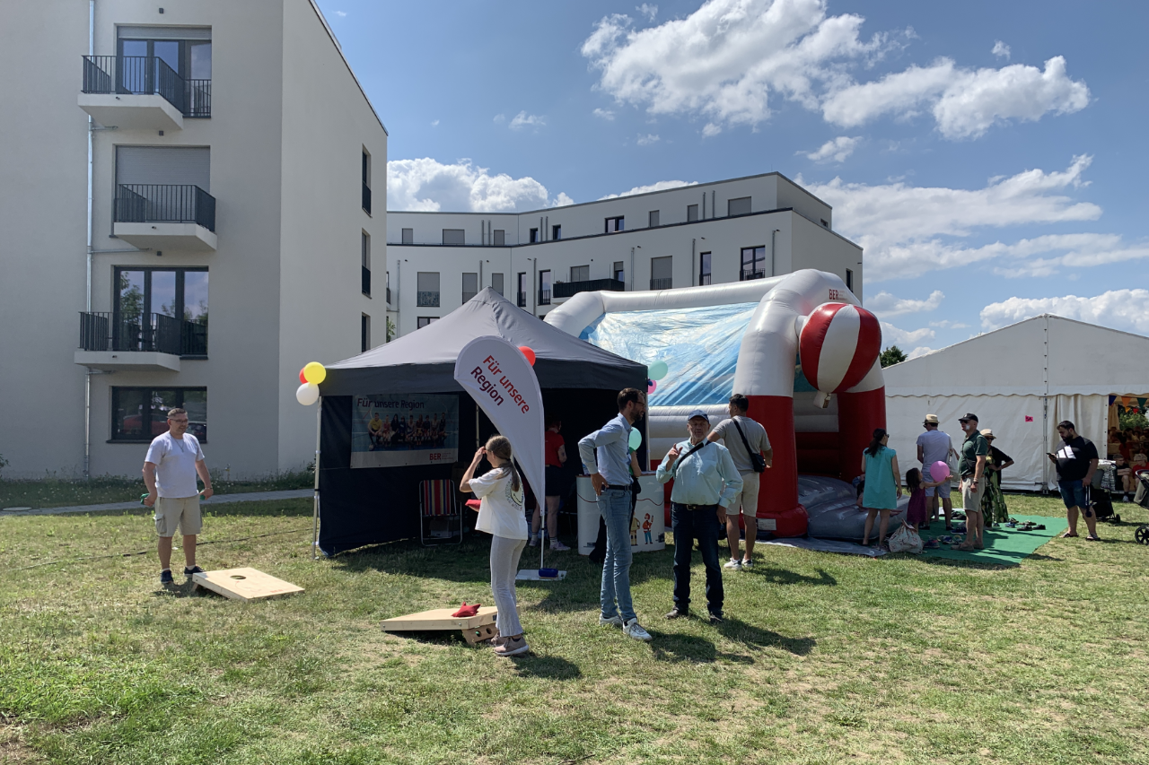 Several people are standing in front of an information stand. A tent and a bouncy castle can be seen in the background.