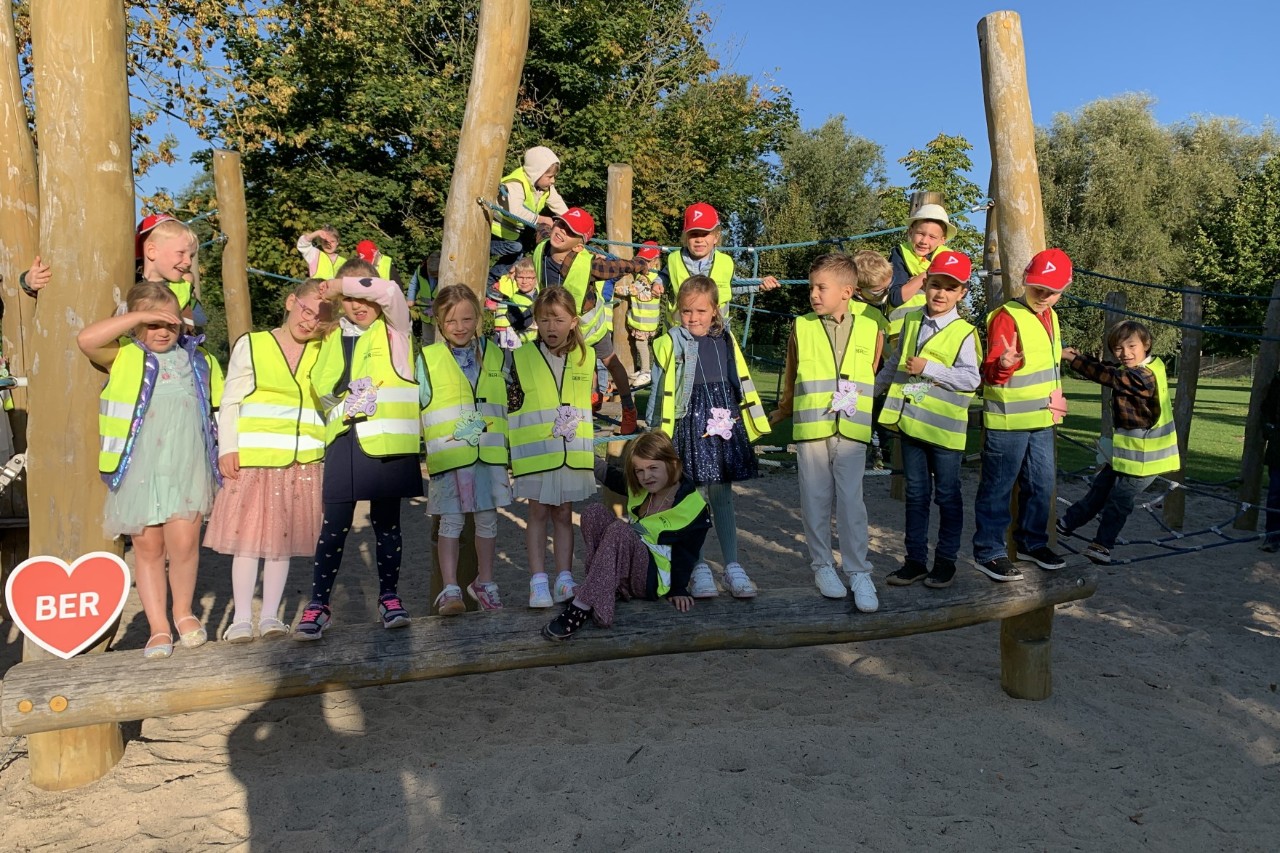 A smaller group of children pose in yellow high-visibility vests on a playground.