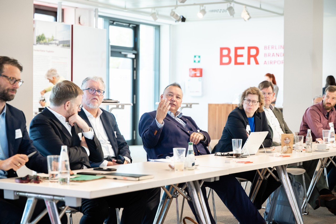 Several people are sitting at a table, one of them is speaking.