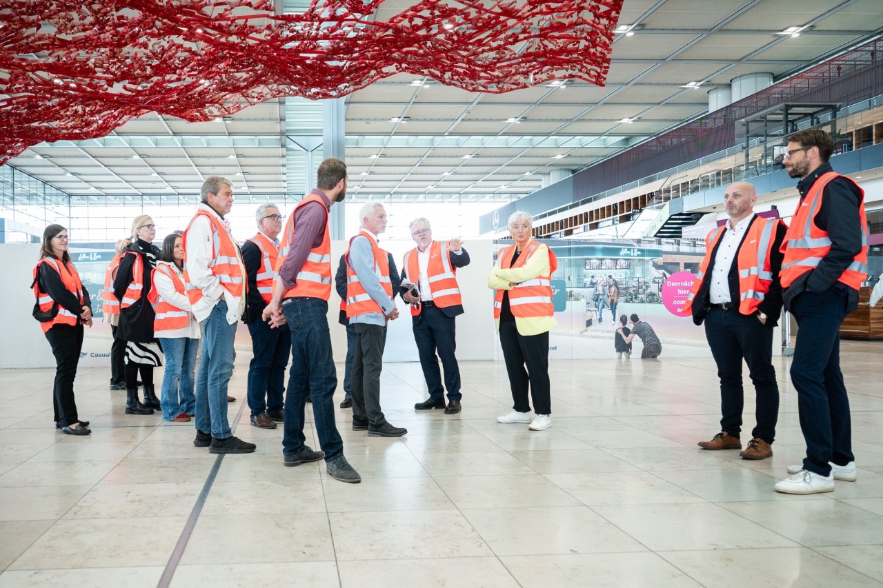 Several people wearing orange-red safety vests are standing in an airport building.