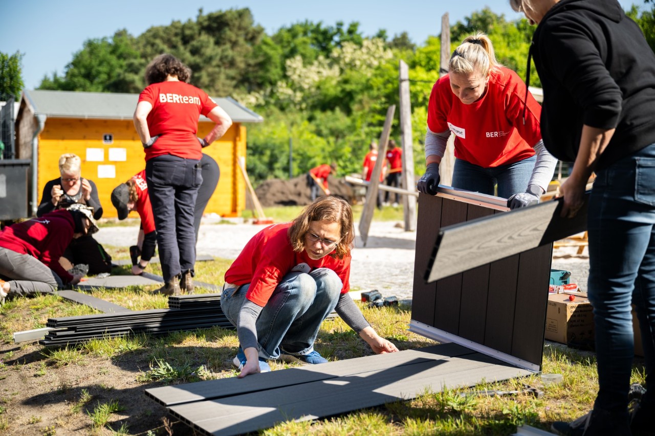A group of people in red T-shirts are assembling wooden boxes.