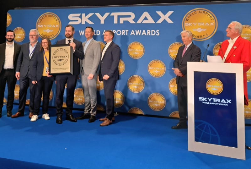Several people in a picture with a badge. Behind them is a background with the Skytrax logo.