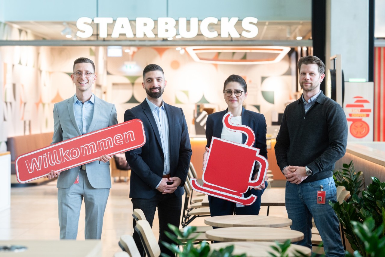Four people are holding signs and smiling at the camera.