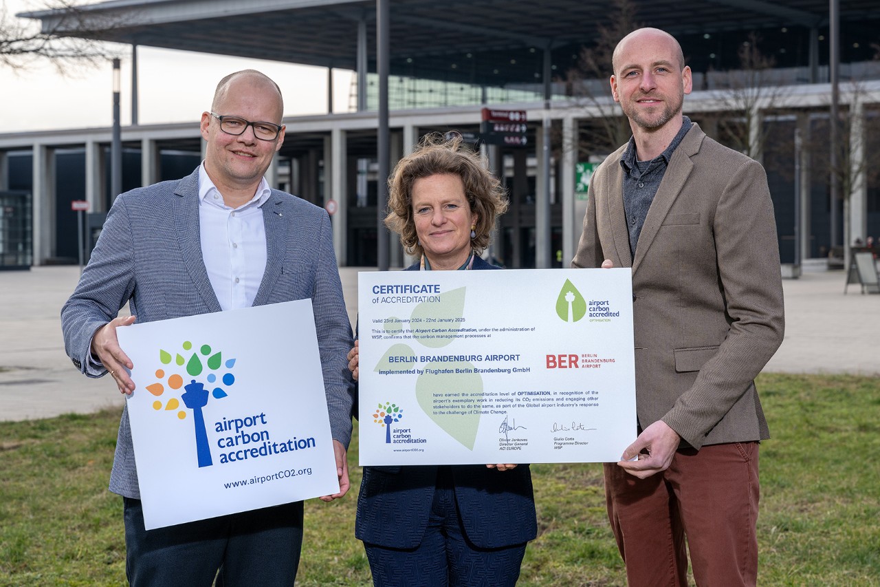 Three people are standing in front of the terminal holding awards in their hands.