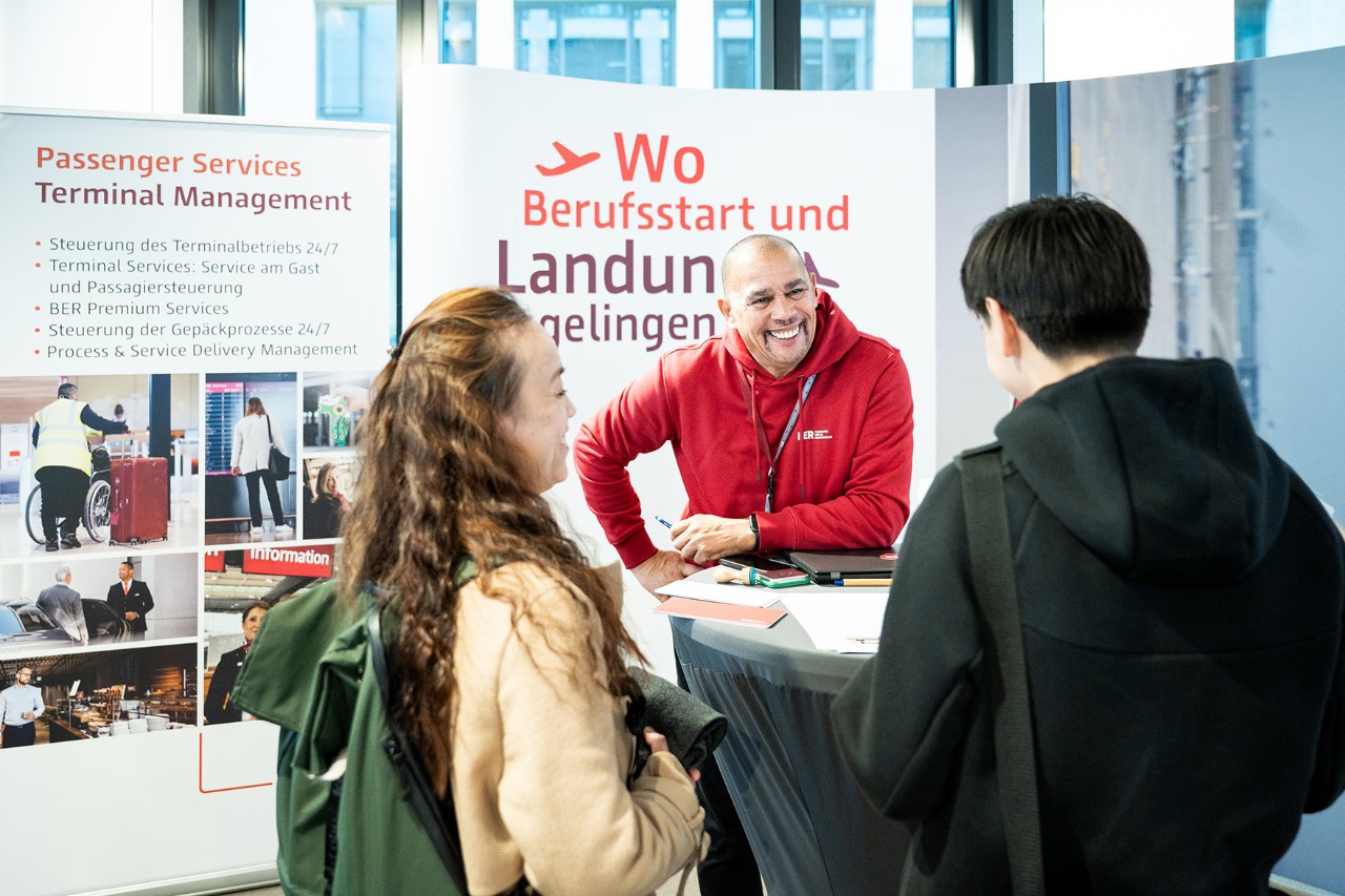Three people are chatting happily in front of an FBB training information stand.