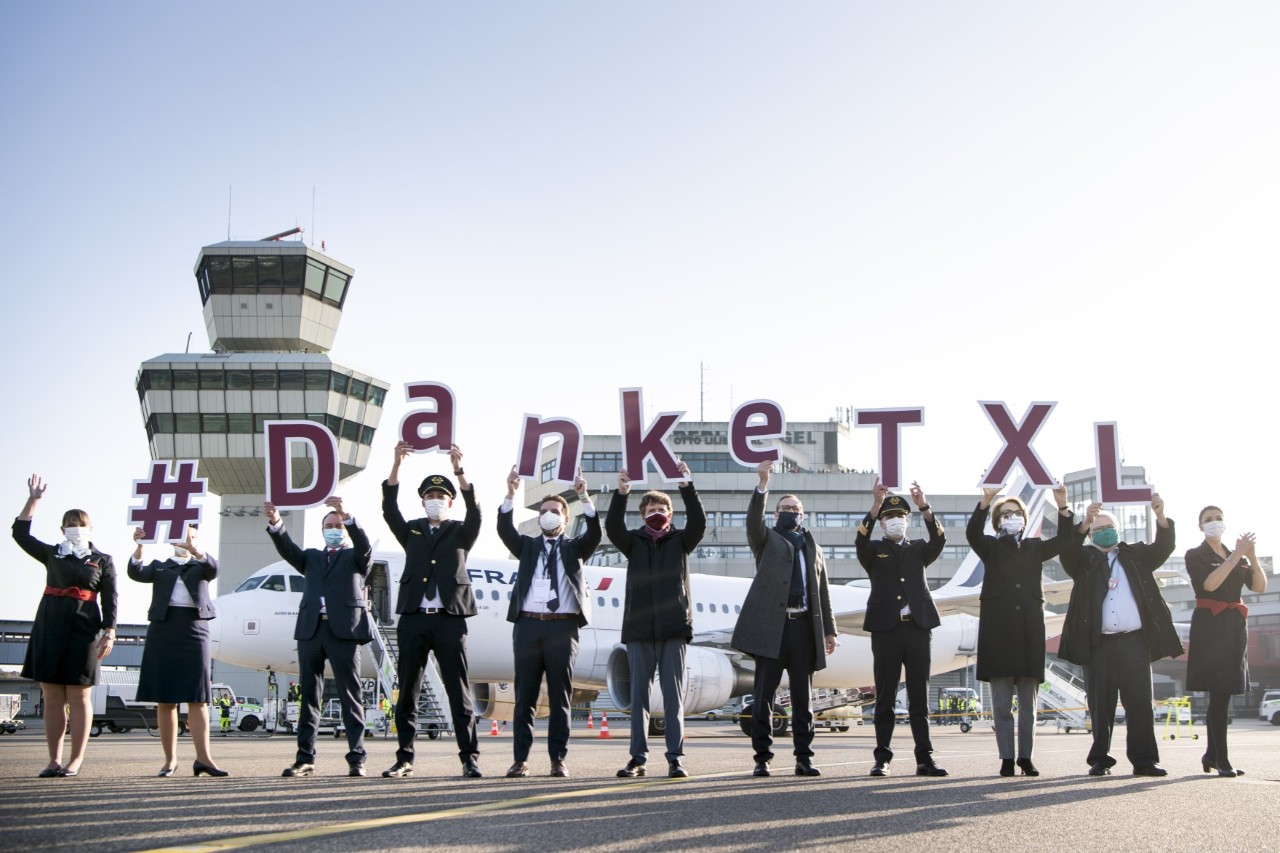 Several people stand in a row holding up signs with letters on them. They say ‘#DankeTXL’ (Thank you, TXL).