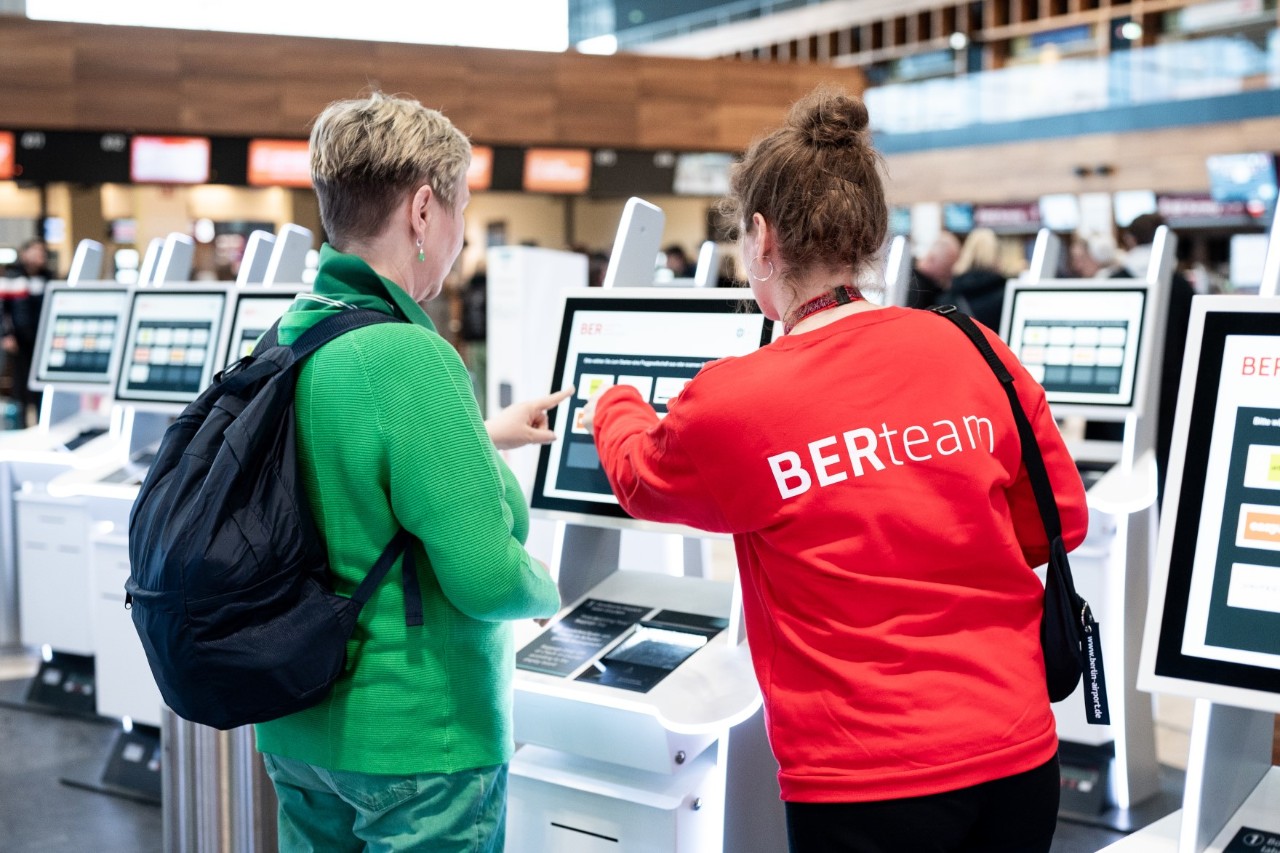 A woman in a red jumper is showing something on a screen to another person.
