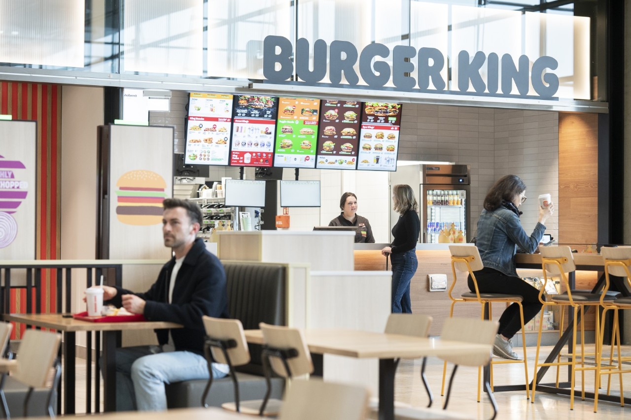 Counter of a Burger King branch; in the foreground tables and chairs where people sit and eat